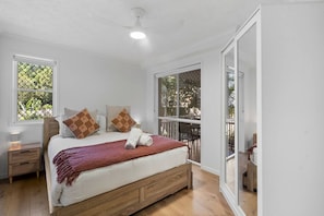 Un dormitorio con cama, dos mesitas de noche, un ventilador de techo y ventanas amplias.