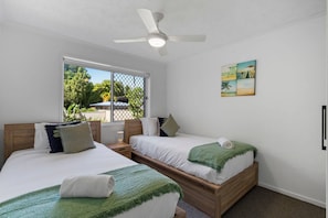 Un dormitorio con dos camas, un ventilador de techo, una ventana con vistas y un cuadro en la pared.