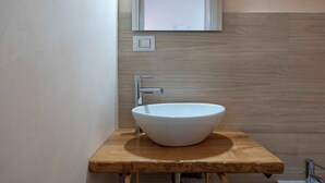 Un baño con un lavamanos blanco tipo recipiente, encimera de madera y un espejo arriba.
