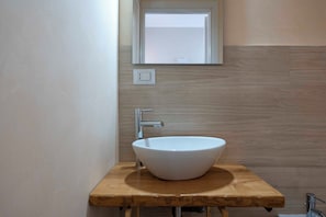 Une salle de bain avec un lavabo sur colonne blanc, un plan de toilette en bois et un miroir au-dessus.