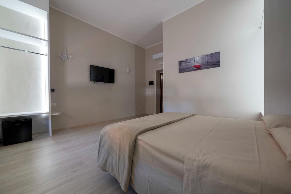 Ein Schlafzimmer mit einem Bett, einem an der Wand montierten Fernseher und einem Fenster.