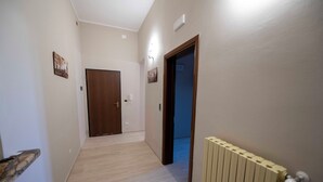 Un pasillo con suelo de madera, un radiador y una puerta al final.