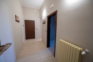 A hallway with a wooden floor, a radiator, and a door at the end. - B&B Teresita (Gallipoli)