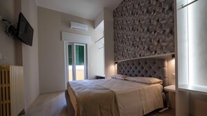 Un dormitorio con cama, televisor de pared, radiador y pared con estampado geométrico.