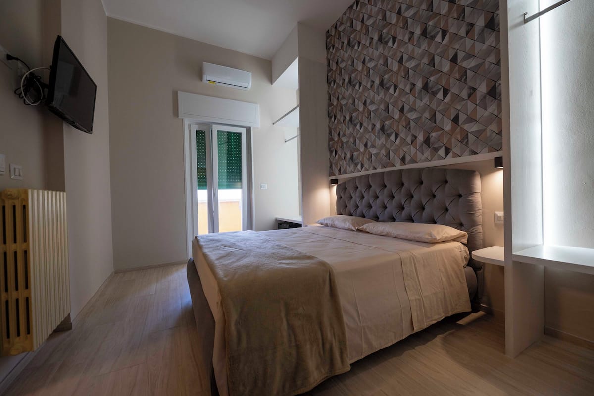 Ein Schlafzimmer mit einem Bett, einem an der Wand montierten Fernseher, einem Heizkörper und einer Wand mit geometrischem Muster.