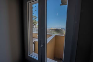 Une vue à travers la fenêtre d’un balcon, avec une balustrade, un cadre de porte et un ciel dégagé.