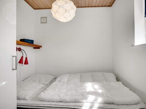 A bedroom with a bed, a hanging light fixture, a shelf with items, and a window. - 4 Star Holiday Home in Lokken (Lokken)