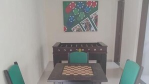 Un pequeño comedor con una mesa y cuatro sillas, un tablero de ajedrez y un cuadro colorido en la pared.