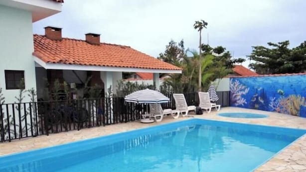 Una piscina con sillones de descanso y sombrillas, rodeada por una terraza de piedra y una cerca.