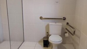 Un baño con inodoro, bidé, barra de apoyo y cabina de ducha de vidrio.