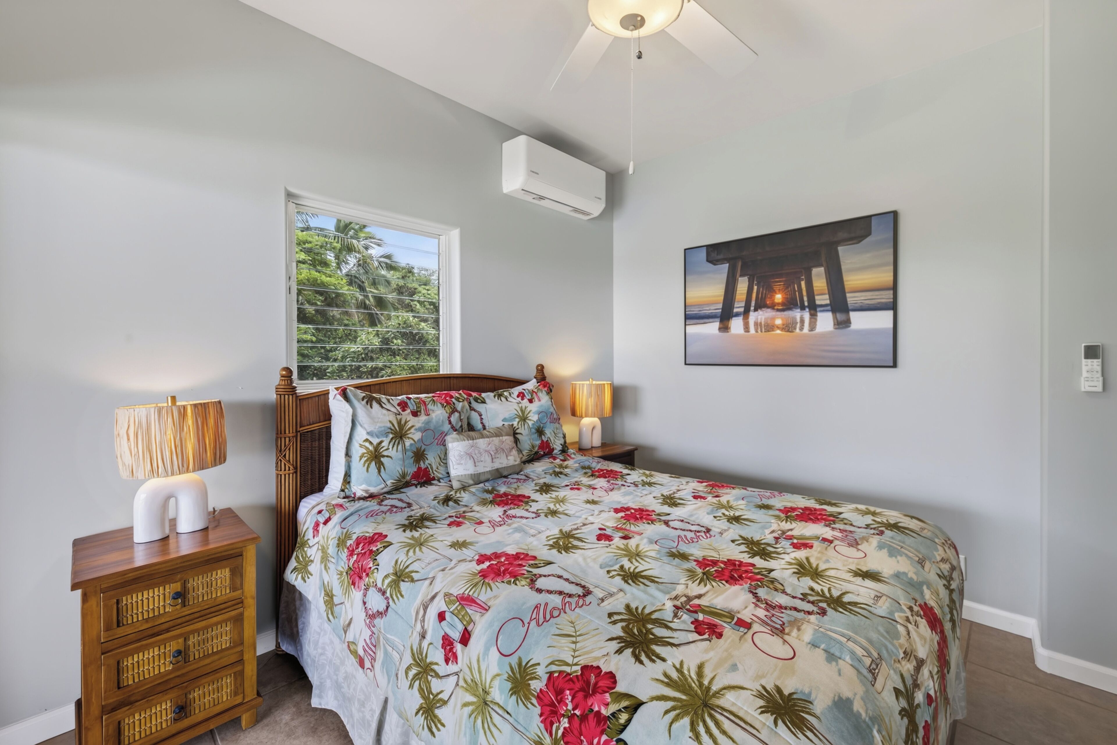 A bedroom with a bed, a nightstand, a lamp, a wall-mounted air conditioner, and a framed picture.