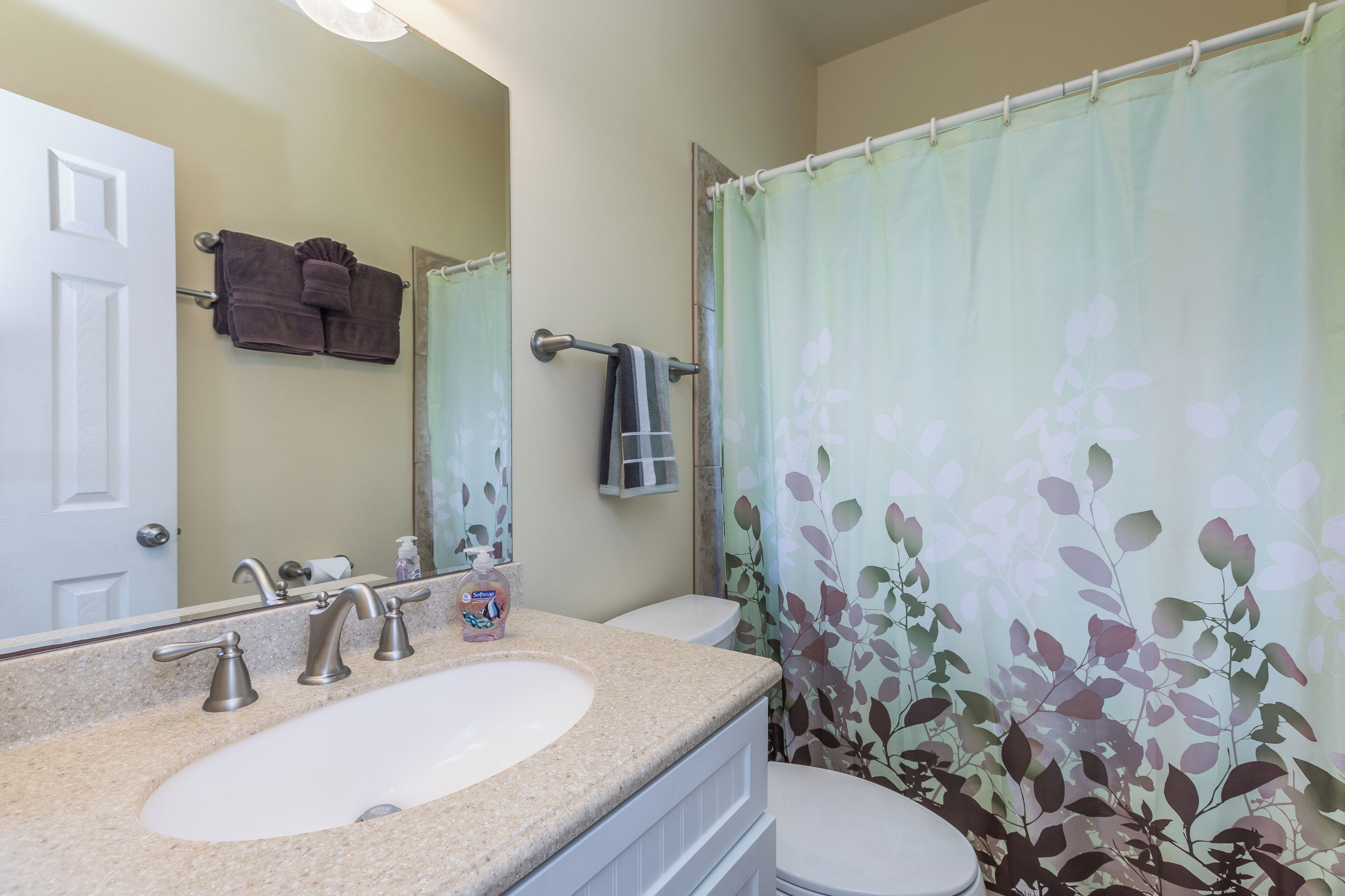 A bathroom with a sink, two faucets, a mirror, a toilet, and a shower curtain with a floral pattern.
