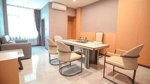 A modern hotel room with a dining table, four chairs, a sofa, and a large window with curtains. - Room-velin Pattaya Hotel-central Pattaya (Pattaya)