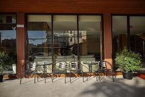Un bâtiment doté de grandes fenêtres en verre, d’une façade en bois et d’un espace extérieur aménagé avec des chaises et des tables en métal.