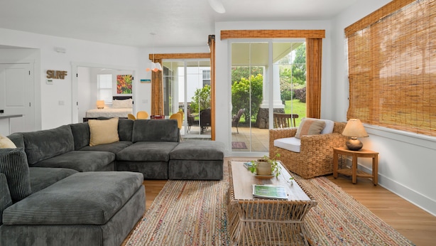 A modern living room with a sectional sofa, a coffee table, and a wicker chair. - Modern 2br Princeville Condo, Pool, Hot Tub, Fitness Center (Princeville)
