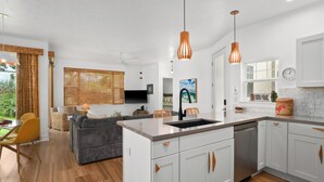 A modern kitchen with white cabinets, a central island, and pendant lighting. - Modern 2br Princeville Condo, Pool, Hot Tub, Fitness Center (Princeville)