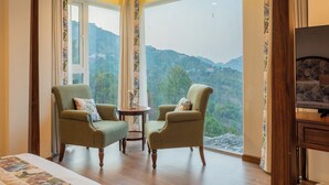 A room with two armchairs, a small table, a television, and a large window offering a view of a mountainous landscape. - ELIVAAS privé Royce Cottage 4BHK Villa (Kasauli)