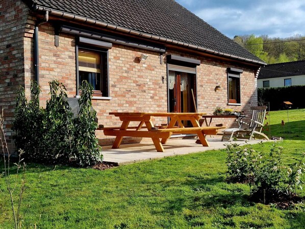 A brick house with a wooden picnic table and a chair outside.