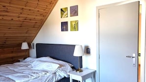 Ein Schlafzimmer mit einem Bett, Nachttischlampen, einem kleinen Tisch, einer Tür und Wandbildern.