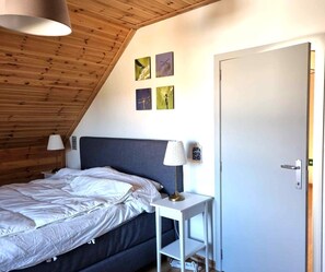 A bedroom with a bed, bedside lamps, a small table, a door, and wall art.