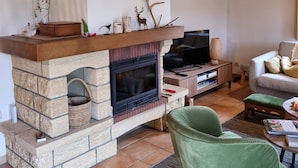 Ein Wohnzimmer mit Kamin aus Stein, einem Fernseher, einem grünen Sessel und einem Sofa.