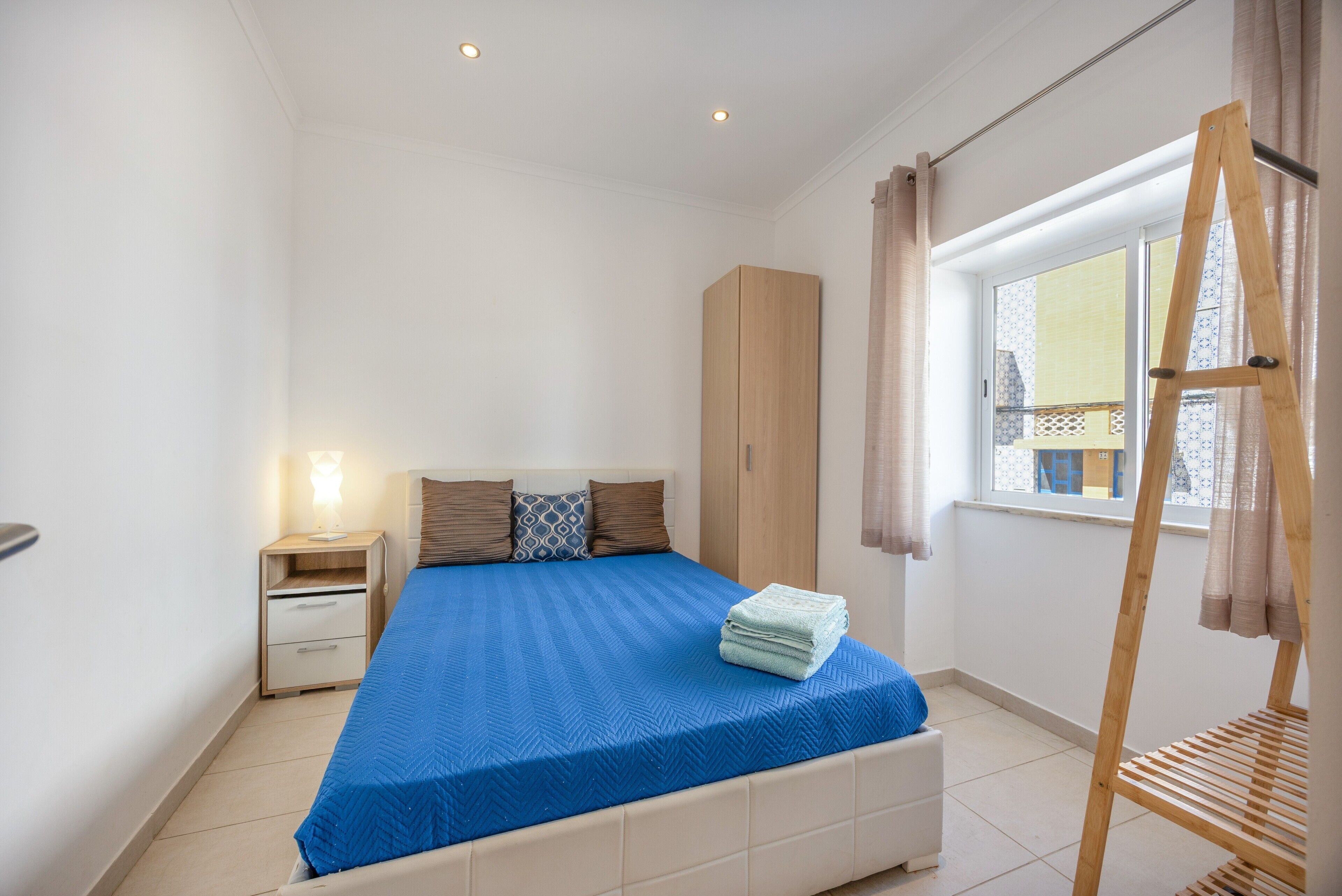 A bedroom with a bed, a wardrobe, a nightstand, a window with curtains, and a wooden ladder.