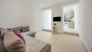 A modern living room with a sofa, a flat-screen TV, and a kitchen in the background. - Holiday Home 'Lanzarote' with Private Terrace, Wi-Fi and Air Conditioning (Alvor)