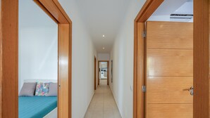 A hallway with a bed on the left, a wardrobe on the right, and a kitchen in the background. - Holiday Home 'Lanzarote' with Private Terrace, Wi-Fi and Air Conditioning (Alvor)