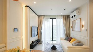 A modern living room with a sofa, a coffee table, a TV, and a large window with curtains. - Magnolia Vinhomes Apartment (Ho Chi Minh City)