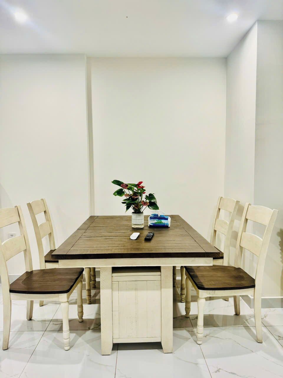 A dining table with four chairs, a vase with flowers, and a remote control on the table.