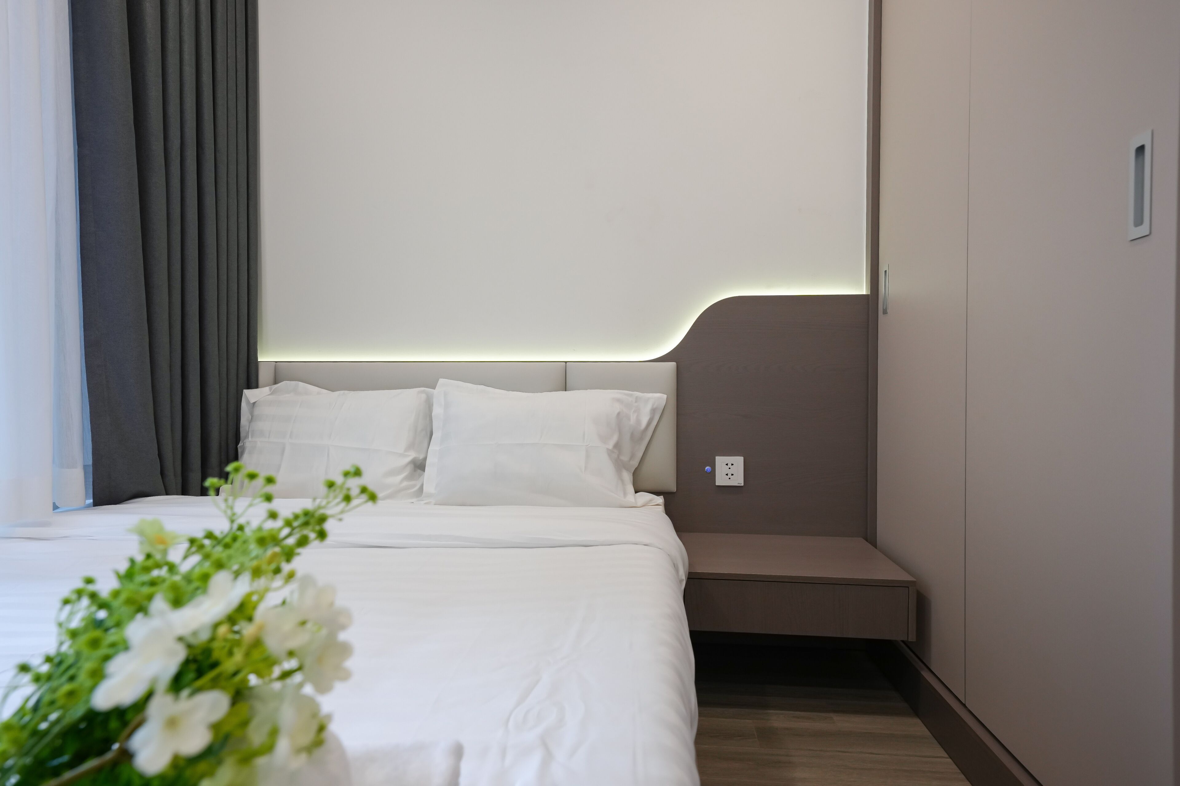 Une chambre d’hôtel moderne avec un lit bien fait, une table de chevet et une prise de courant fixée au mur.