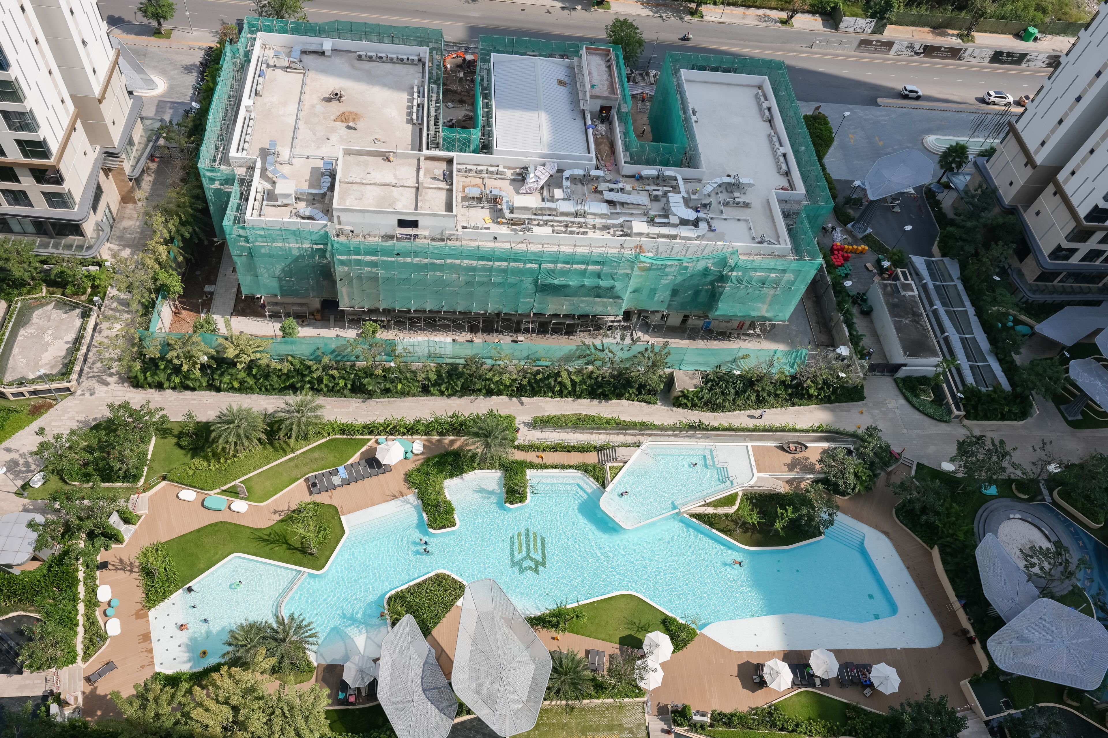 A multi-story building with a rooftop terrace, surrounded by landscaped gardens and a swimming pool.