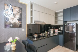 A modern kitchen with a central island, black appliances, and a marble backsplash. - Magnolia Vinhomes Apartment (Ho Chi Minh City)