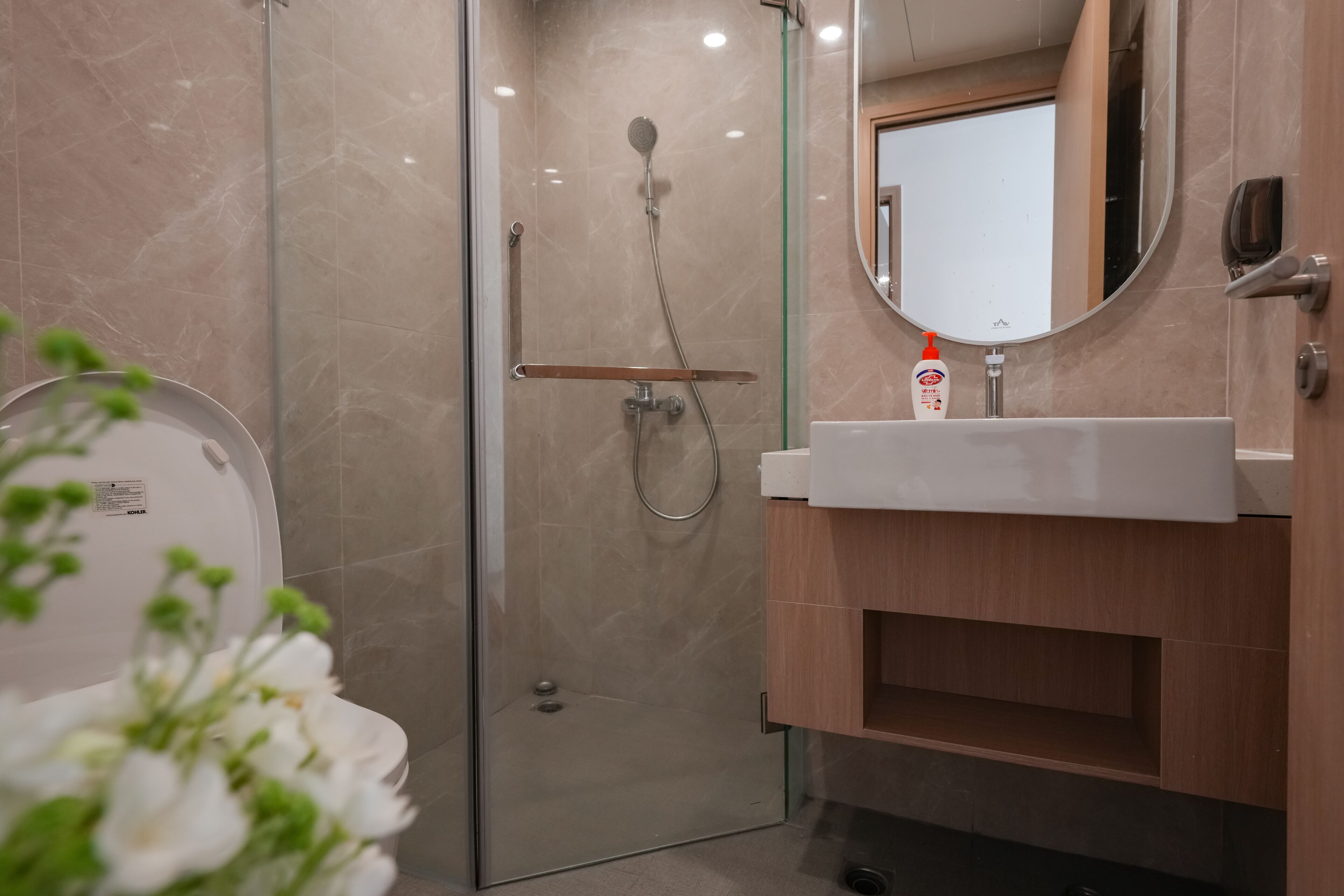 Et moderne badeværelse med en glasafskærmet brusekabine, toilet og et spejl over vasken.
