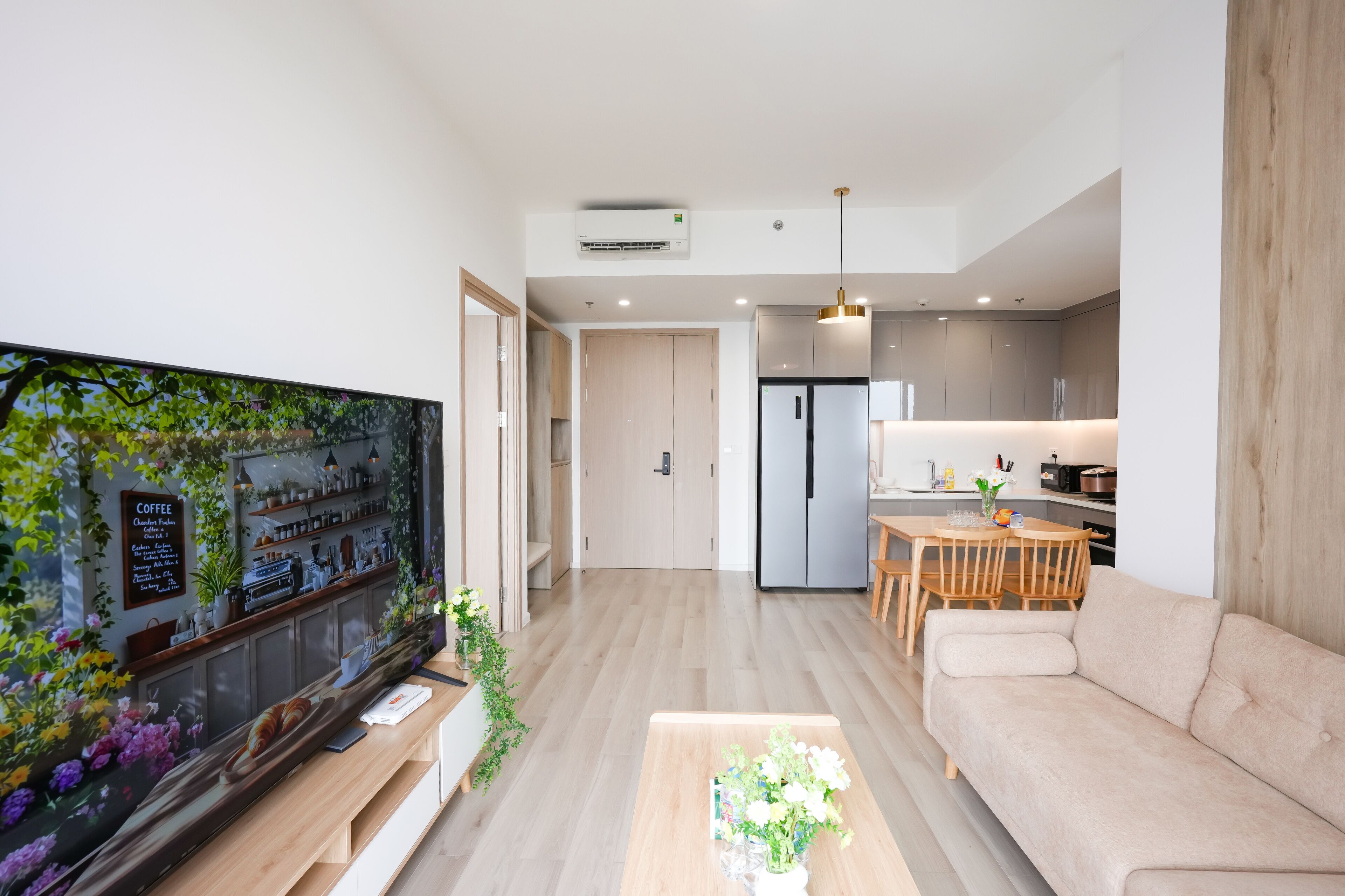 A modern living room with a flat-screen TV, a sofa, a coffee table, and a kitchen area with a dining table and chairs.