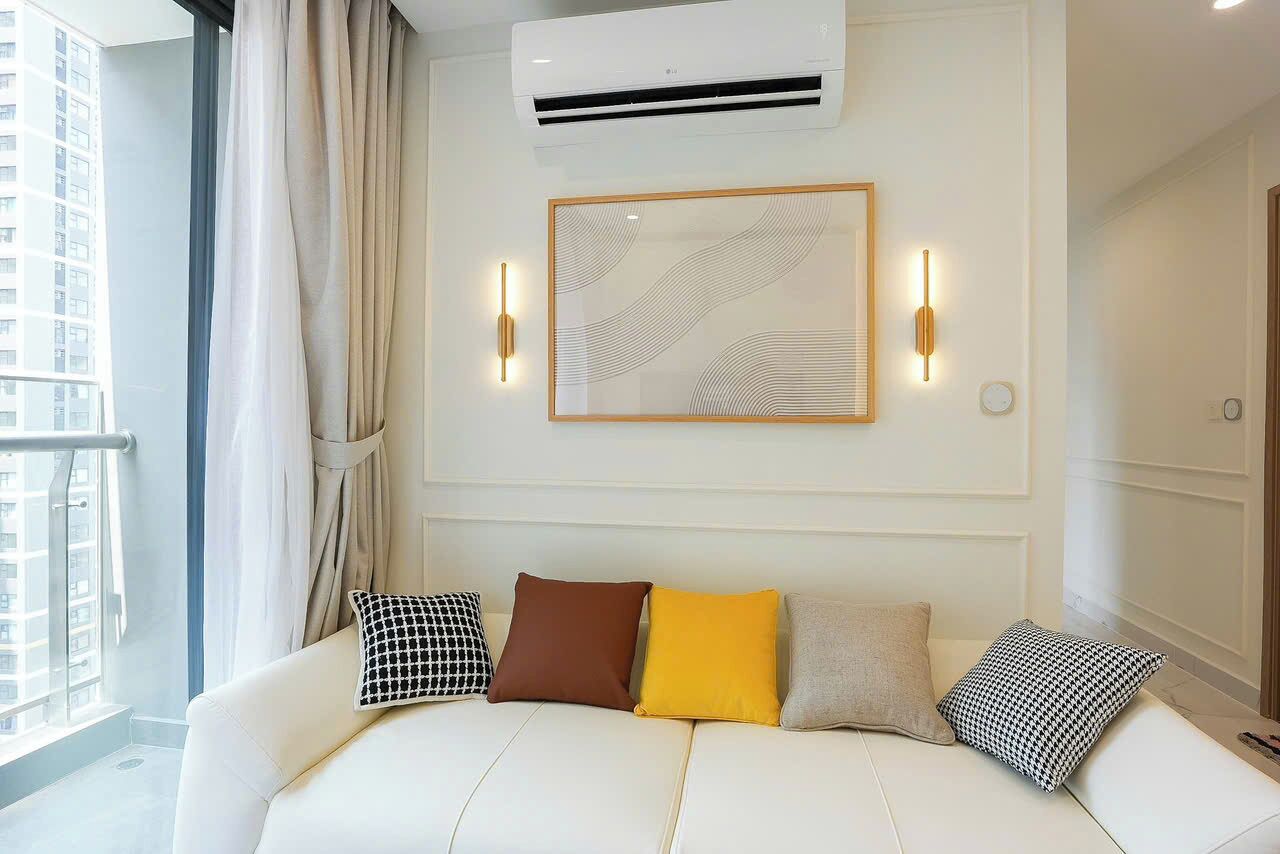 A hotel room with a white sofa, a framed abstract artwork, and a window with curtains.