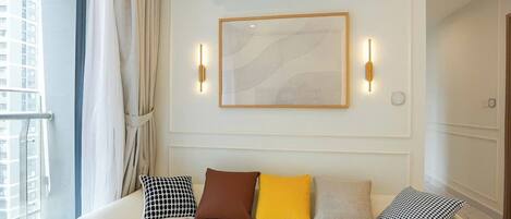 A hotel room with a white sofa, a framed abstract artwork, and a window with curtains.