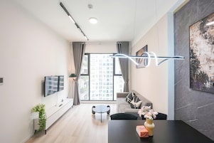 Uma sala de estar moderna com sofá, mesa de jantar, TV fixada na parede e uma grande janela com cortinas.