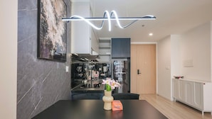 A modern kitchen with a dining area, a vase with flowers, and a neon light. - Magnolia Vinhomes Apartment (Ho Chi Minh City)
