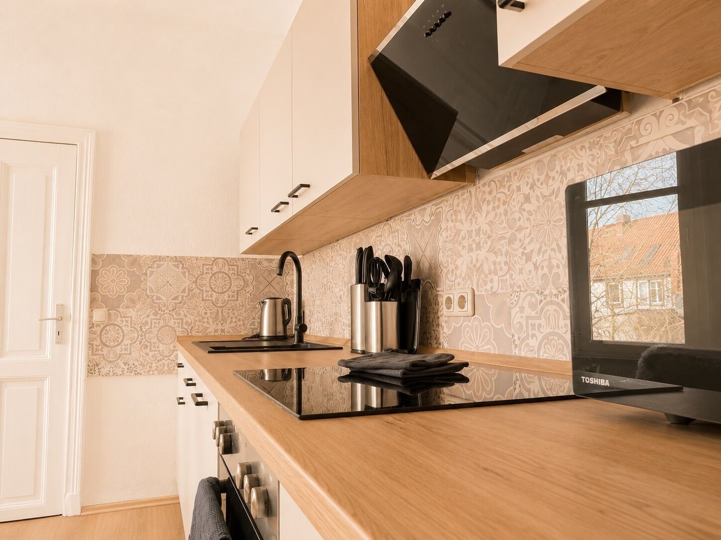 A modern kitchen with a black stove, stainless steel kettle, and knife holder.