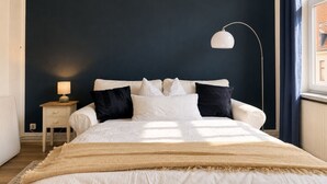 A bedroom with a bed, bedside table, lamp, and a view of the outside. - Maritime old town apartment Wismar with WLAN and workstation - 2 rooms (Wismar)