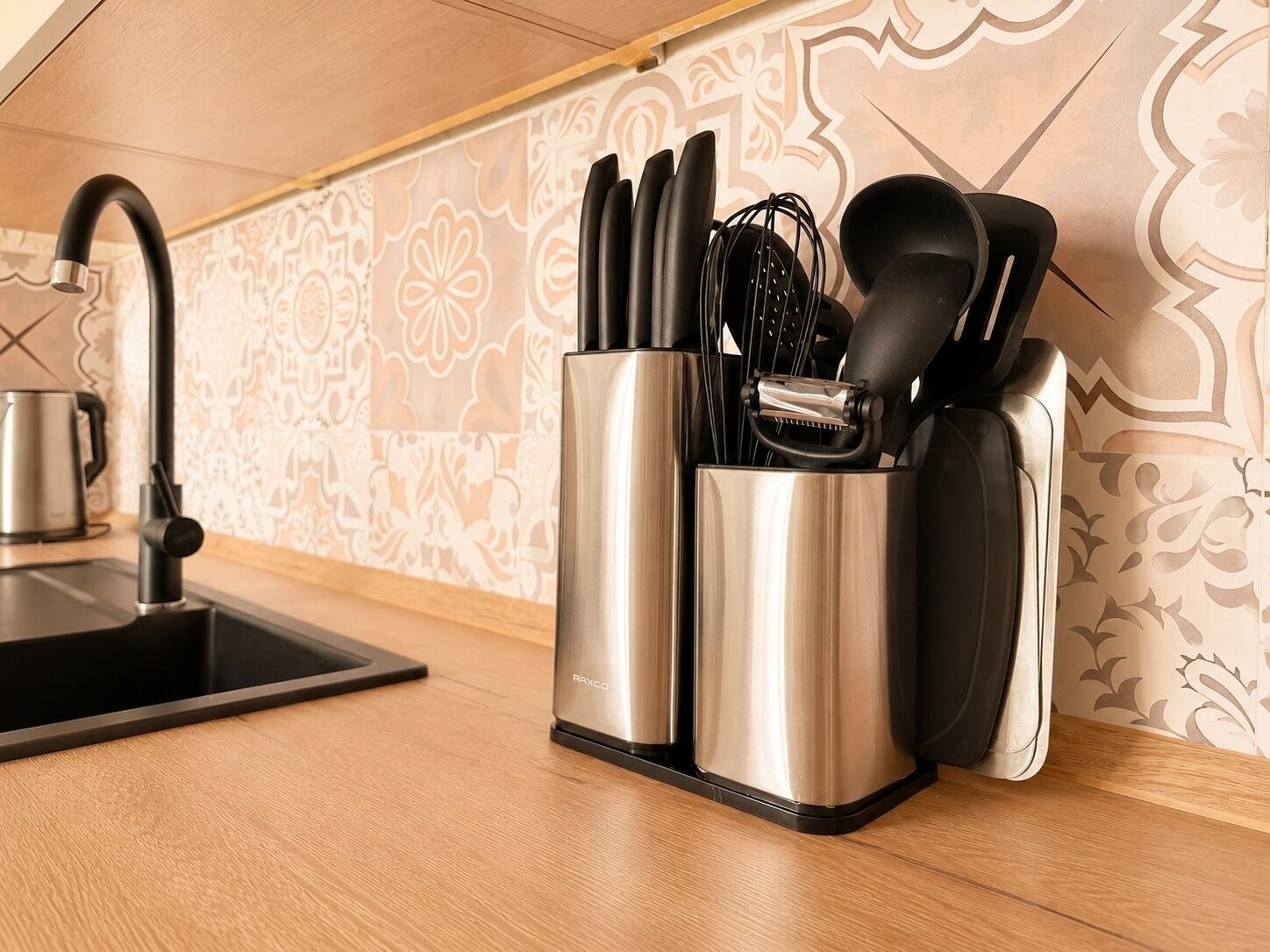 A kitchen with a modern faucet, a stainless steel utensil holder, and a patterned backsplash.