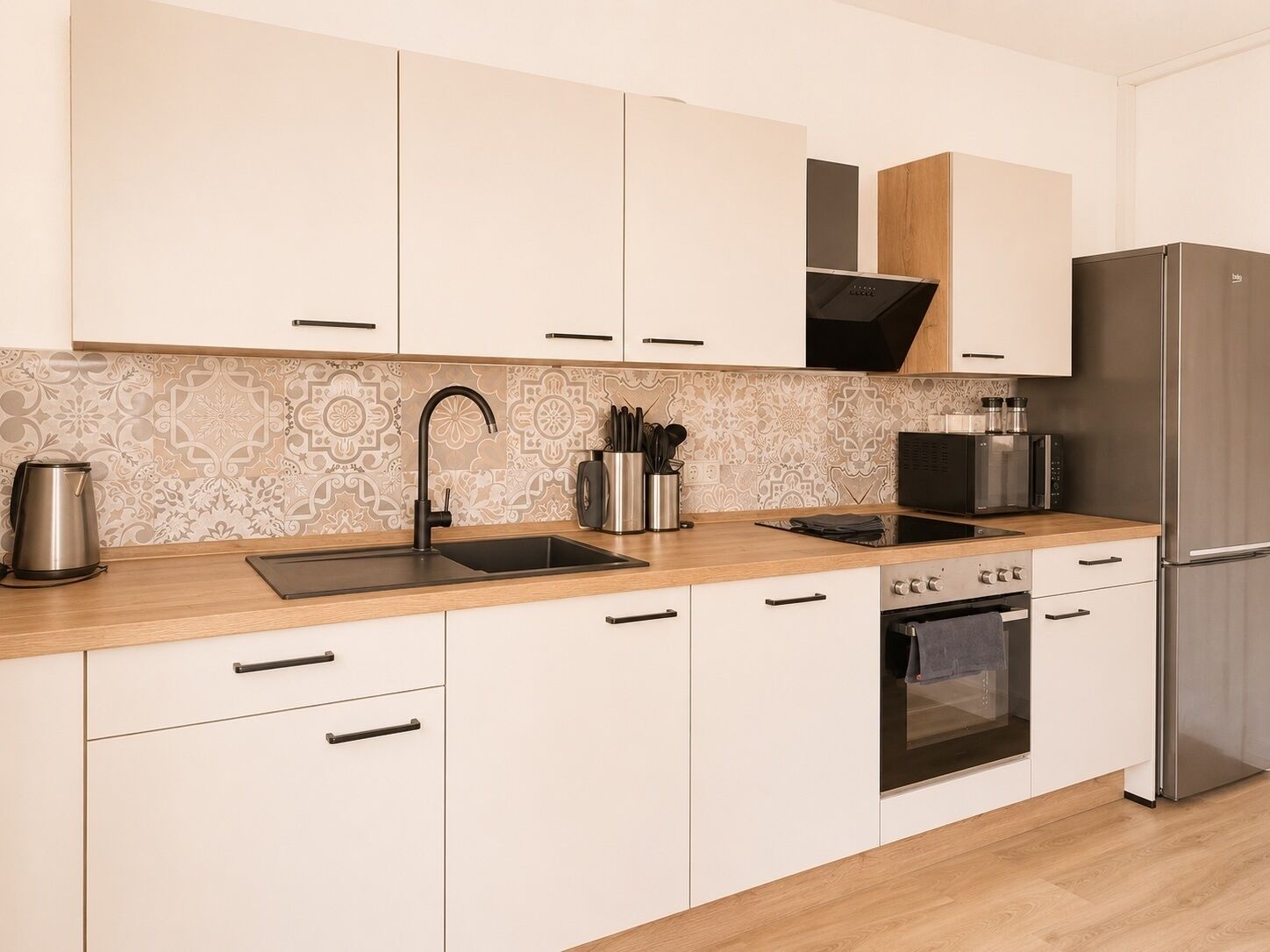 A modern kitchen with white cabinets, a stainless steel sink, and a built-in oven.