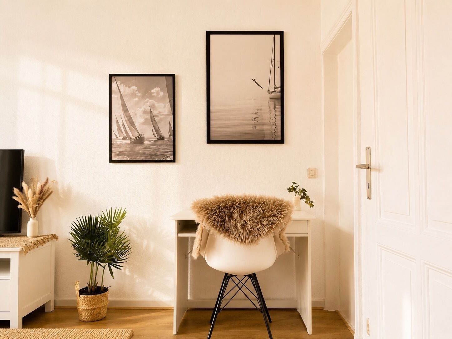 A room with a white door, a desk with a chair, two framed pictures on the wall, a potted plant, and a television on a stand.