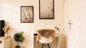 A room with a white door, a desk with a chair, two framed pictures on the wall, a potted plant, and a television on a stand.