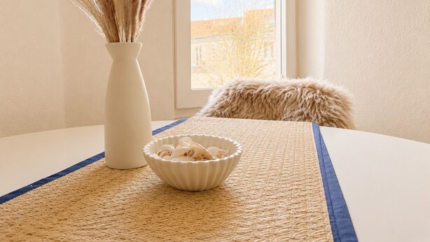 A room with a woven placemat, a white vase with dried plants, and a white bowl on the table. - Maritime old town apartment Wismar with WLAN and workstation - 2 rooms (Wismar)