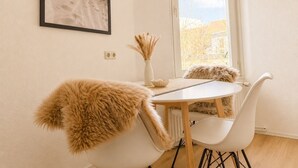 A dining area with a round table, white chairs, and a window with a view of buildings. - Maritime old town apartment Wismar with WLAN and workstation - 2 rooms (Wismar)