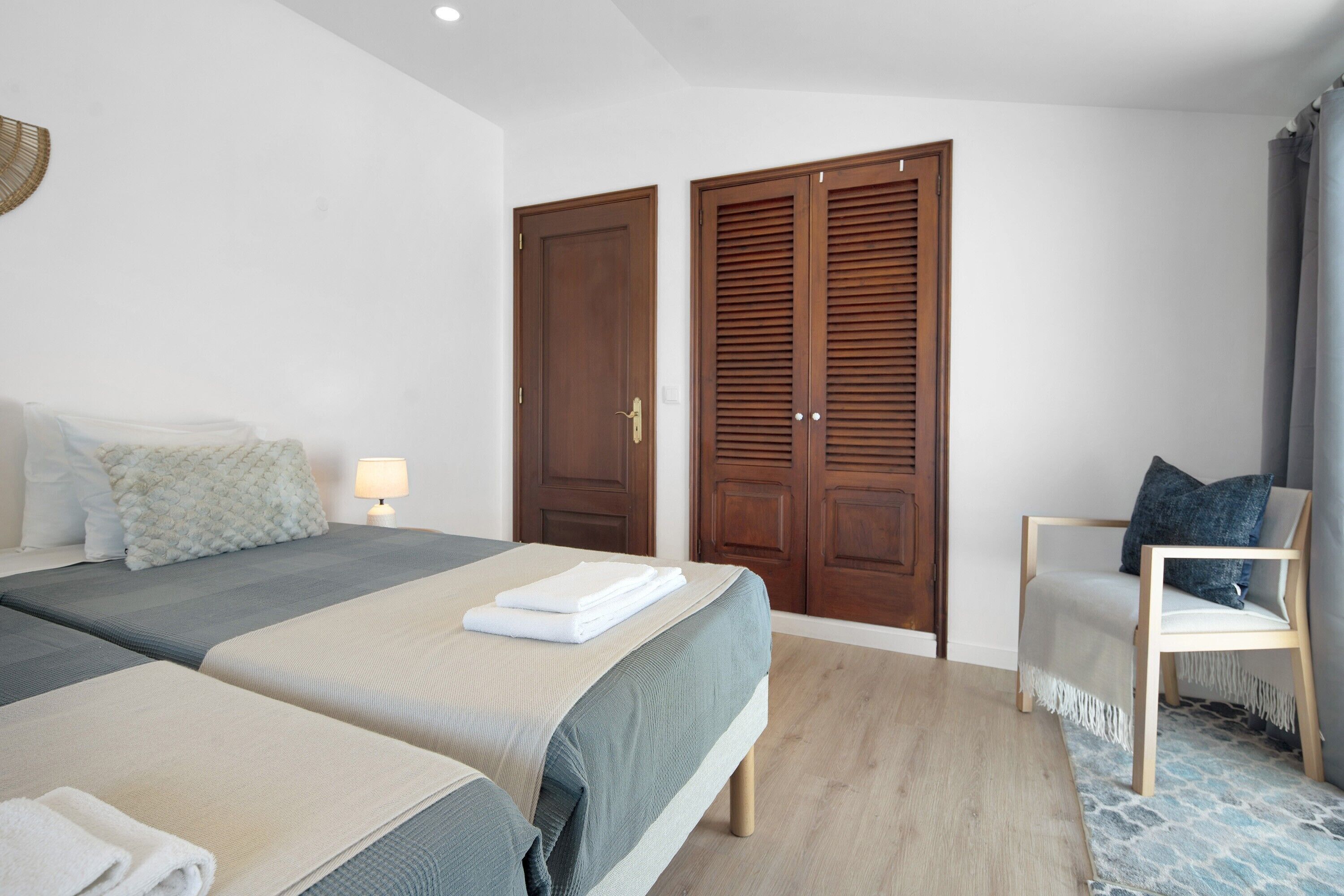 Een hotelkamer met twee bedden, een stoel, houten kasten en een betegelde vloer.