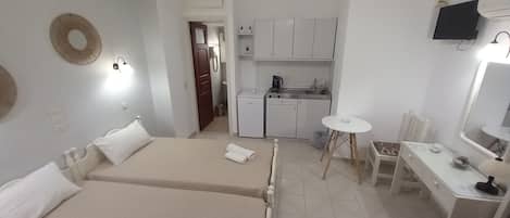 Habitación de hotel con dos camas, una kitchenette pequeña, zona de comedor y baño.