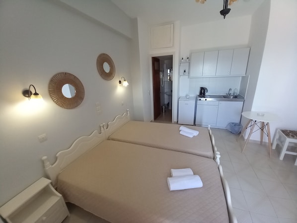 A hotel room with two beds, a kitchenette, a small table, and a bathroom visible through an open door. - DIAMOND VIEW (Lesvos)